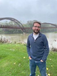 a man standing in front of a bridge over a river